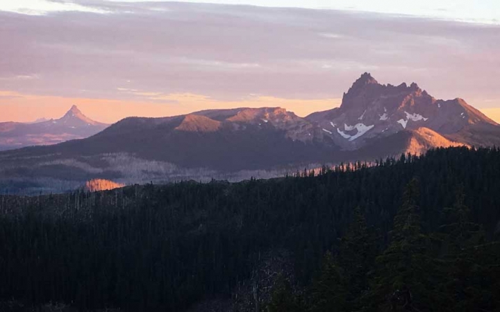 A mountainous landscape appears purple and pink while the sun is either setting or rising. 